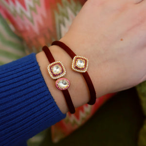 Close-up of a hand wearing a burgundy diamond bracelet with decorative elements on a patterned fabric background.